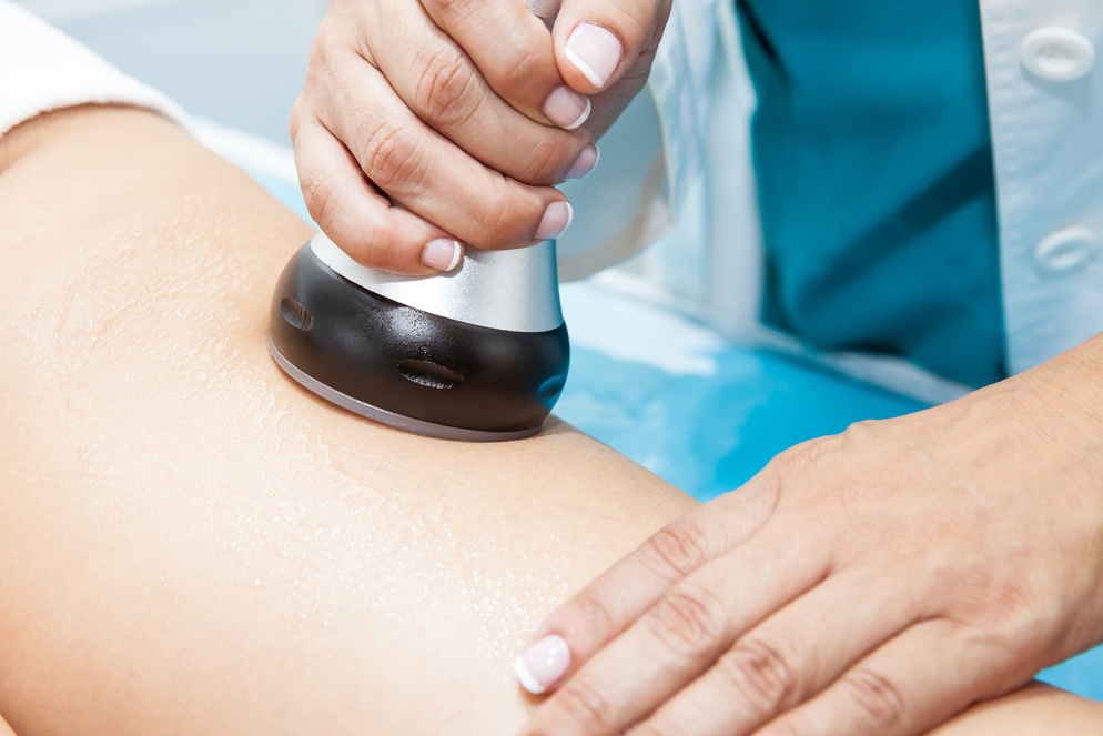 Doctor performing an  ultracavitation treatment on a young female patient leg